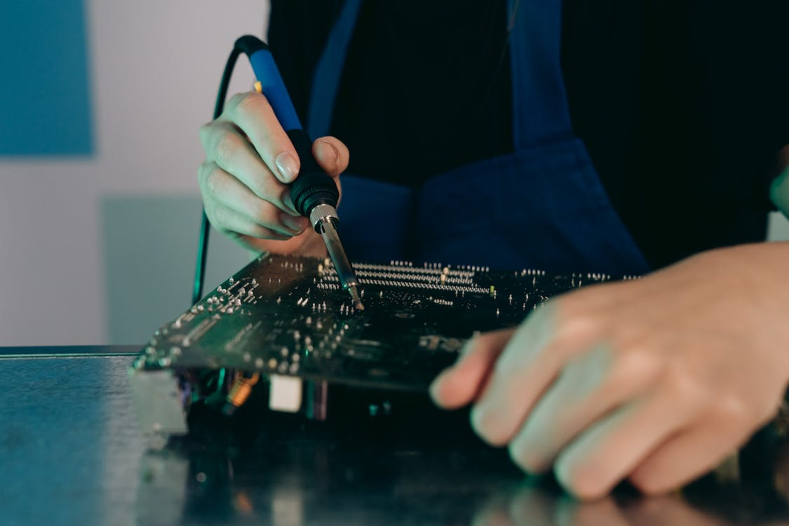 A person is using a solder iron on a PCB
